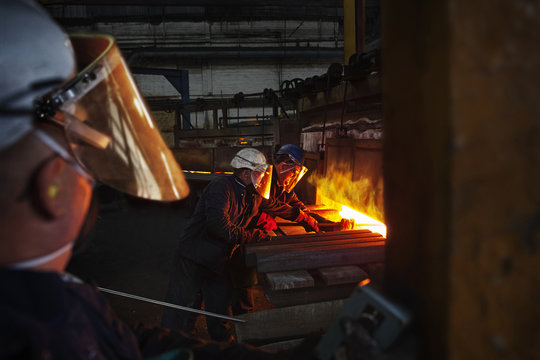 100mm square steel billet is removed from furnace as cold steel billet waits to be heated, with furnace door operator in foreground