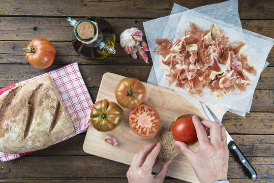 Cocinero untando tomate en una rebanada tostada de pan casero con ajo y aceite de oliva para preparar el tradicional jamón con tumaca