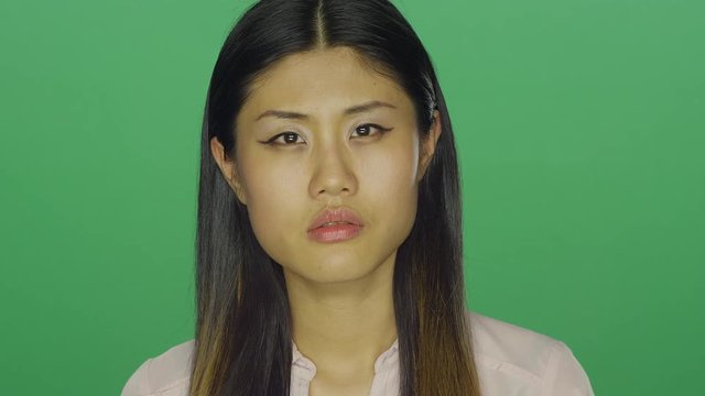 Beautiful Asian woman stares ahead and then smiles, on a green screen studio background 
