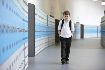 Unhappy schoolboy walking alone in school corridor