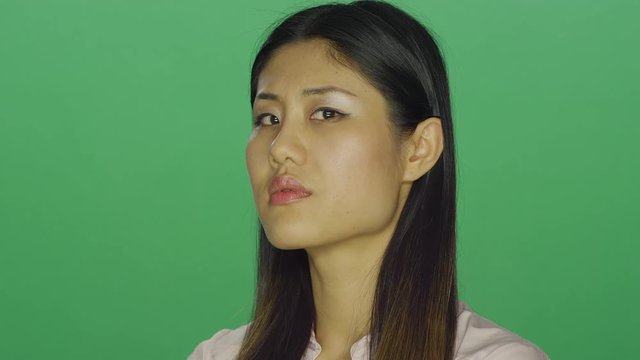 Beautiful Asian woman looks disappointed with her arms crossed, on a green screen studio background 