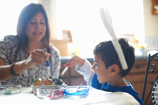 Woman and boy wearing bunny ears painting Easter eggs