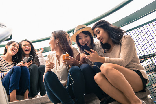 Five young women sitting on steps looking at smartphones