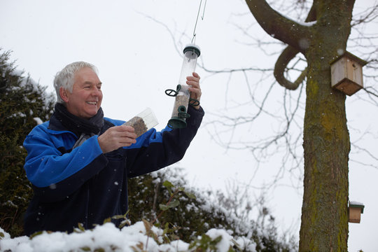 Senior man filling bird feeders in garden in winter