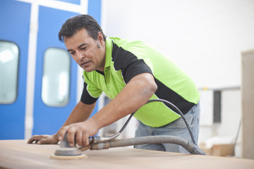 Man sanding down plank of wood in carpenters workshop