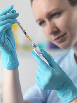 Healthworker holding up a syringe and vial, and filling the syringe in preparation for carrying out an injection
