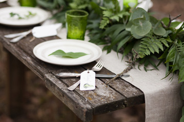 White plate with green leave and silver spoon and fork with blank label on wooden table and linen tablecloth