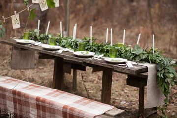 Weddind table setting with white plates and green glasses decorated with white candles, green leaves and eucalyptus outdoors