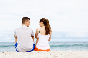 Young couple looking at each other while sitting on beach