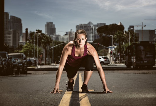 Young adult woman in start position in road, getting ready to run