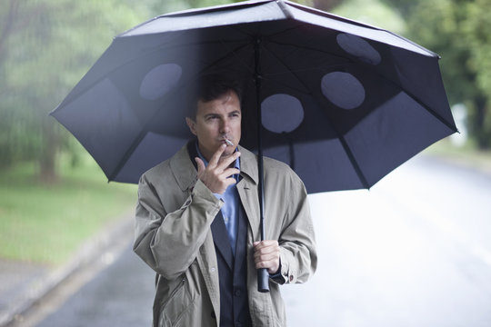 Businessman smoking cigarette under umbrella