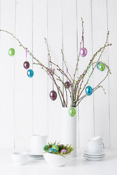 Still life of crockery and shiny easter eggs hanging from twigs
