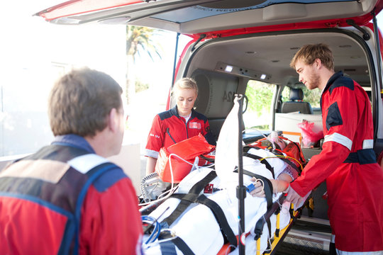 Paramedics lifting woman on stretcher into ambulance