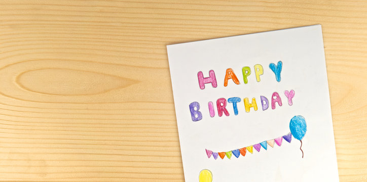 Happy birthday card kid handwriting on wood background. Children or baby draw and paint colorful text with imagine on white paper. For fill text on mock-up.