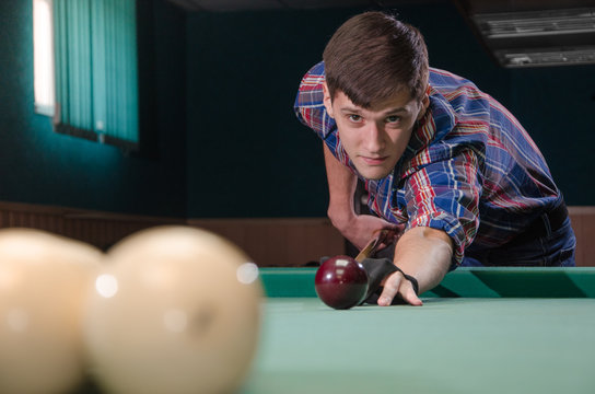 boy in focus aiming for shot the billiard ball which aren't in focus