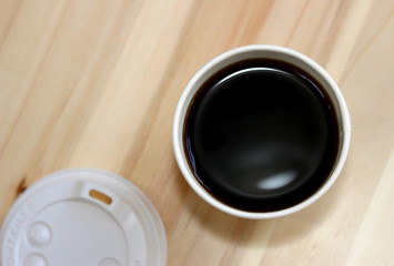 Top view of a paper cup of black coffee on wooden table