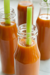 Natural and fresh carrot juice in small bottles with fresh celery on light background