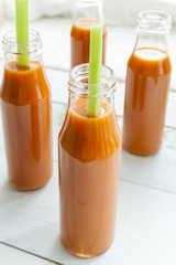 Natural and fresh carrot juice in small bottles with fresh celery on light background