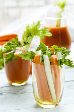 Fresh carrots and celery in glass with fresh carrot juice and parsley on black background