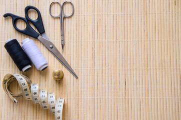 Sewing accessories on beige background with copyspace. Scissors,centimetre bobbins with thread and needles .