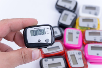 Digital pedometer in the hand over pile of pedometers