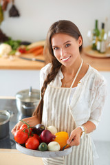 Smiling young woman holding vegetables standing in kitchen