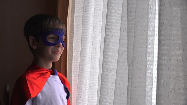 boy in a superhero suit looks out the window and waits