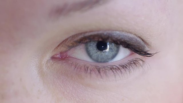 Big close up of a woman's blue-grey eye looking at the camera and looking around.  Looping clip, recorded in 4K.