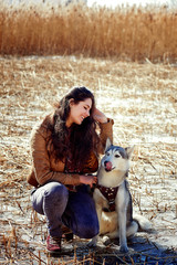 Naklejka na ściany i meble Beautiful woman with husky outdoors.Happy brunette woman with smiling siberian husky dog, sitting in a poppy field on a sunny day, on a walk with dog