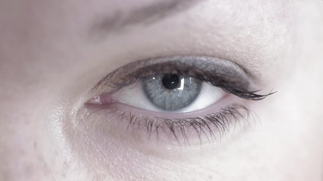 Big close up of a woman's blue-grey eye looking at the camera and looking around.  Loopable clip, recorded in 4K at 60fps