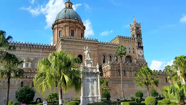 The Impressive Architecture of The Ancient Cathedral of Santa Maria Assunta in Palermo. Dome on The Background of Blue Sky and Clouds. Palm Trees and Statue in Front of The Cathedral.