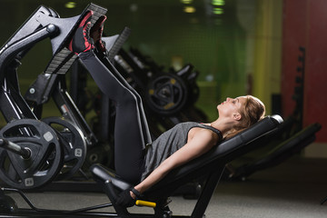 Fototapeta na wymiar Sportive woman using weights press machine for legs. Gym.