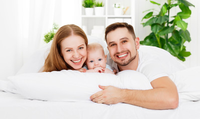 Obraz premium happy family of father, mother and baby playing in bed
