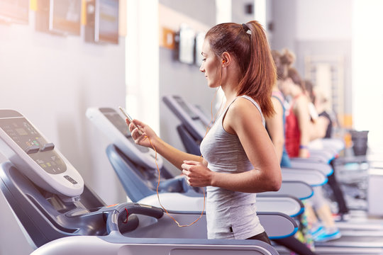 Girl running on the treadmill and listening to music at the gym, soft focus picture