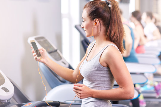 Girl running on the treadmill and listening to music at the gym, soft focus picture