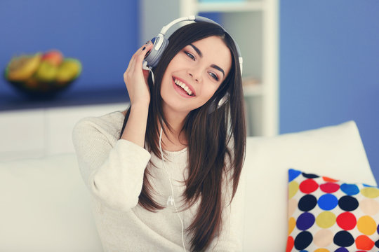 Happy young woman with headphones listening to music on a sofa at home