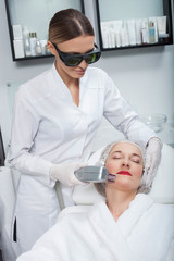 Cheerful cosmetologist is making laser therapy in clinic