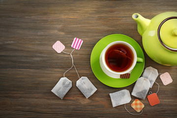 Cup of tea with tea bags and teapot on wooden table background