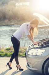 Woman crouching on the road next to a car. Sad person. Damaged car. Natural background. Car accident.