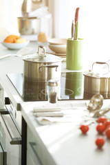 Modern table and electric stove with utensils and vegetables in the kitchen beside window