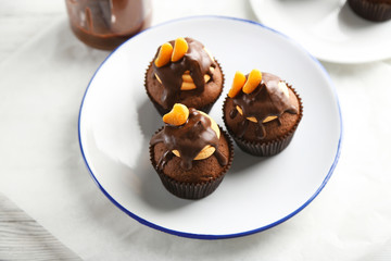 Three tasty cupcakes with slice of mandarin and chocolate on a plate, close up