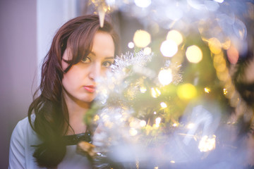 Beautiful young woman stands against christmas tree