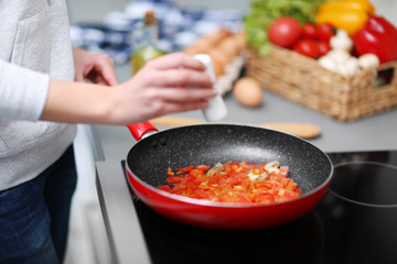 Human hand with salt and frying pan on stove, closeup
