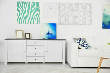 Modern living room interior with white sofa, lockers and canvases on the white wall