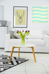 Modern living room interior with white sofa, coffee table, big graphic carpet and canvases on the white wall