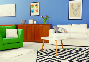 Modern living room interior with white sofa, coffee table, big graphic carpet, green chair and canvases on the blue wall