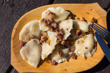 Polish cuisine - dumplings - pierogi ruskie. Homemade dumplings with fried bacon and onion served in wooden dish on wooden table.