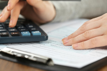 Female hand holding a pen and using calculator while filling in the individual income tax return,...