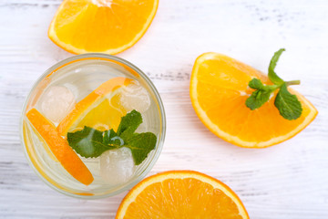 Fresh cocktail with ice, mint and orange on white wooden table background