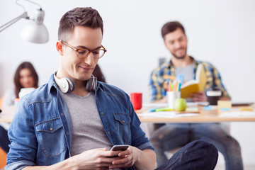 Cheerful young guy is playing with smartphone